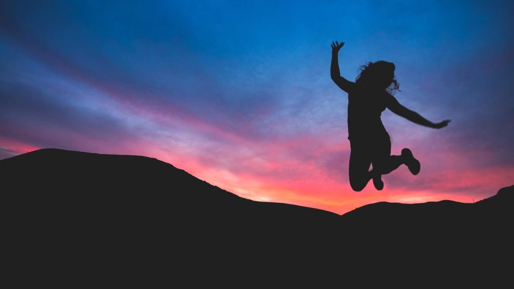 siluett av en glad tjej som hoppar med solnedgång i bakgrunden